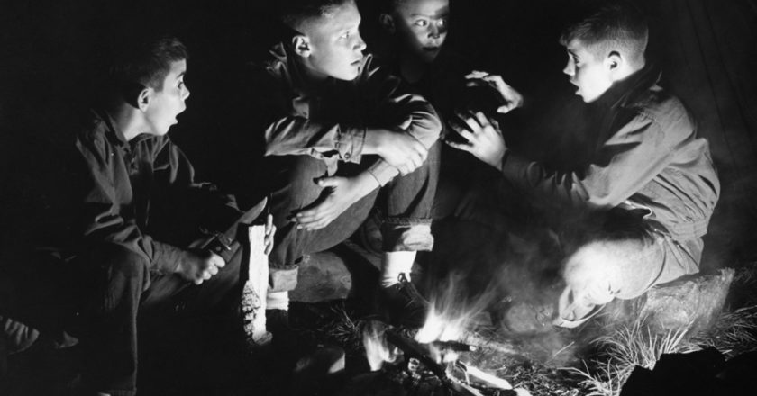 Boys listening to friend telling stories by campfire