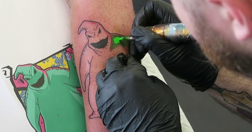 Tattoo artist tattooing The Nightmare Before Christmas' Oogie Boogie on a persons arm