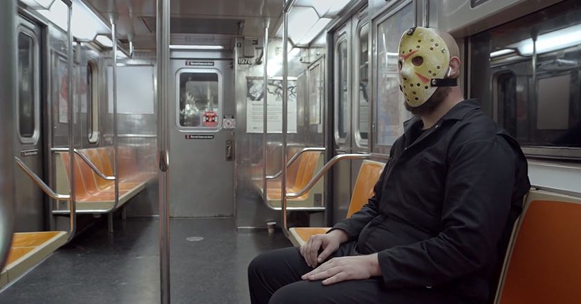 A Jason Voorhees-like character sits alone in a subway car