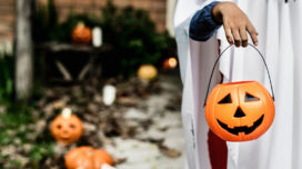 A kid dressed as a ghost trick or treating with a jack-o'-lantern candy pale