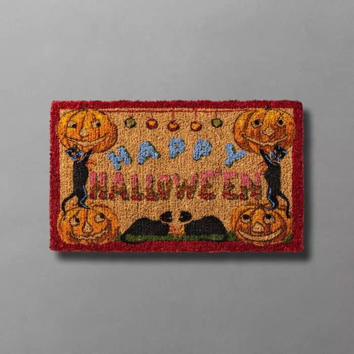 19th century-inspired imagery of pumpkins and black cats on a handwoven door mat