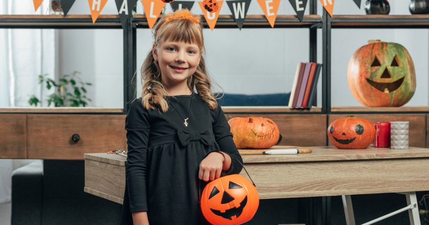 Young girl in a black dress with a trick or treat bucket