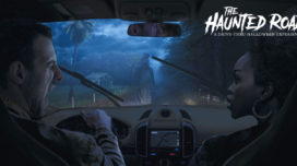 The Haunted Road key art featuring a man and woman in a car with a ghost in a top hat standing in front of them in the road