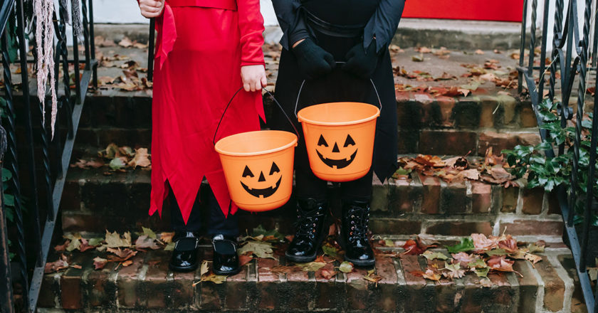 Two kids dressed in a devil and witch costume hold trick or treat buckets