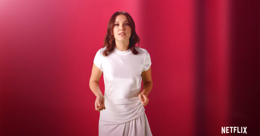 Millie Bobby Brown in a white dress in front of a red background