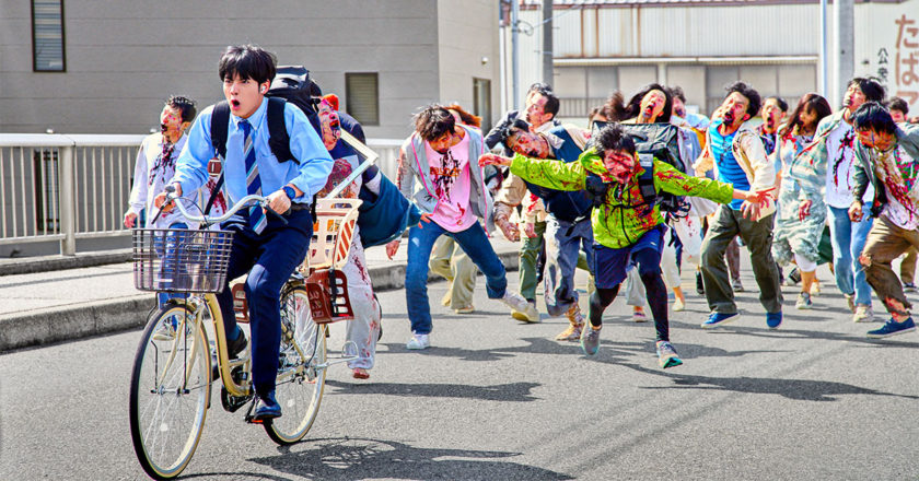 Akiro fleeing a hoard of zombies while riding a bike in Zom 100