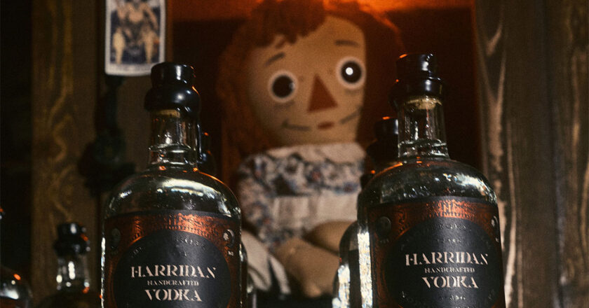 Two bottles of Harridan Vodka Paranormal Reserve sit in front of the case holding the infamous Annabelle doll