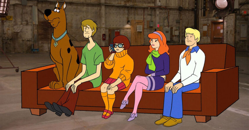 Scooby, Shaggy, Velma, Daphne, and Fred sit on a couch at the Warner Bros. Studios backlot