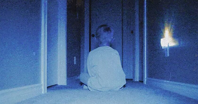 A young boy sits in a dark hallway in "Skinamarink"