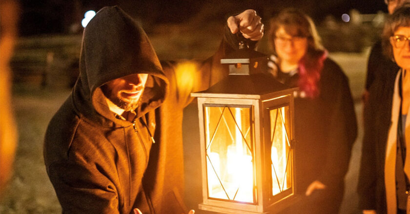 A US Ghost Adventures tour guide holds a large lantern while surrounded by guests