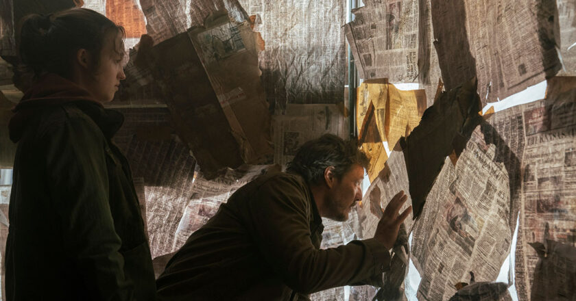 Bella Ramsey as Ellie and Pedro Pascal as Joel look out an opening in a newspaper covered window in episode 4 of "The Last Of Us."