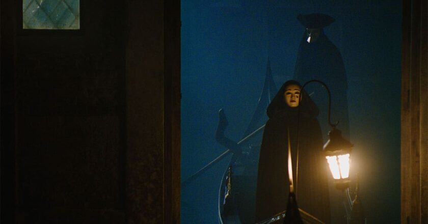Two masked characters stand in a lantern lit gondola from “A Haunting in Venice."
