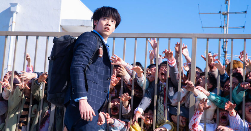 Eiji Akaso looks on as a horde of zombies reaches for him through a gate in “Zom 100: Bucket List of the Dead”