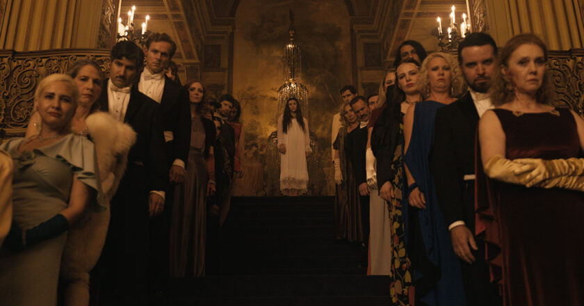 Theater-goers line the aisle as a woman in a white gown stands at the top of the stairs