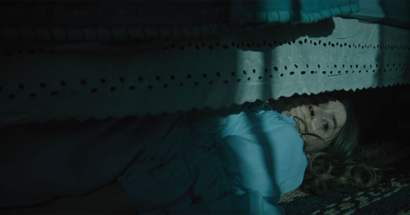 Kaitlyn Dever as Brynn, hides under a bed in a moonlit room.