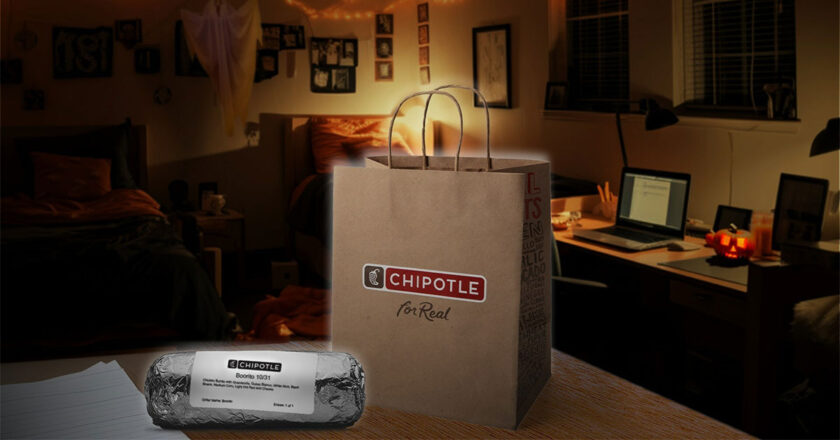 A Chipotle burrito and Chipotle bag on a table in a bedroom at night.