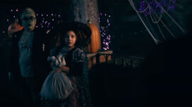 A boy dressed as Frankenstein and a girl dressed as a witch stand in fear as a shadow looks on