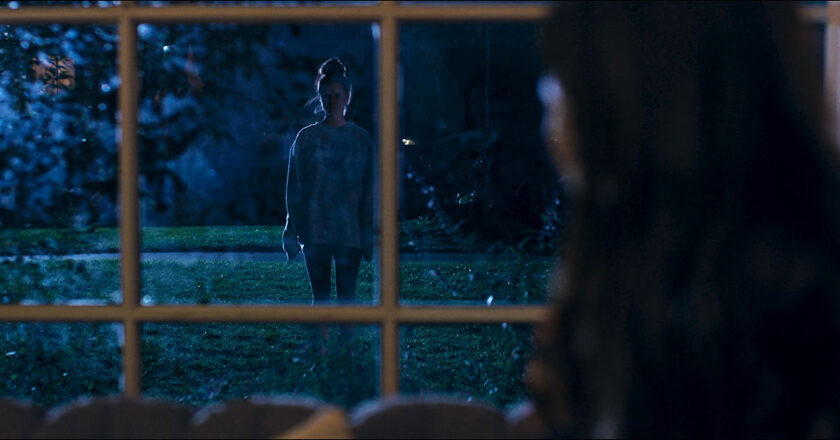 Kimmy stands outside a window at night in a still image from "The Hive"