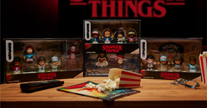 Fisher-Price Little People Collector Stranger Things collection on a table with a remote, a container of popcorn, and a Stranger Things comic book