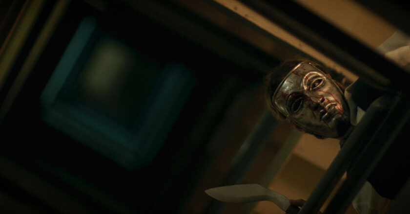 A masked killer holding a knife looks over the railing in a stairwell in "Night of Violence."
