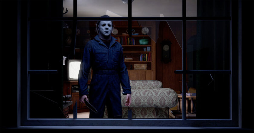 Michael Myers stands holding a knife looking out a broken window