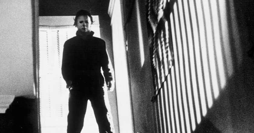 A black and white photo of Michael Myers standing at the top of stairs